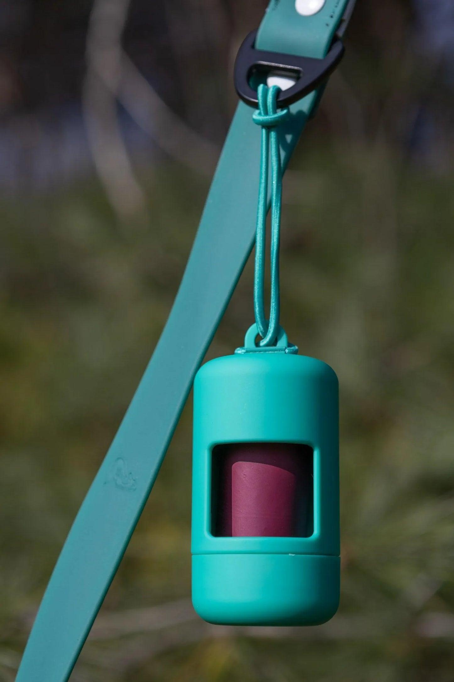 Green dog waste bag holder with pink interior on a blurred natural background