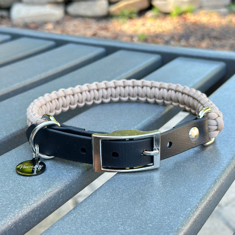 Dog collar with a light tan braided design and black biothane strap on a blue surface.