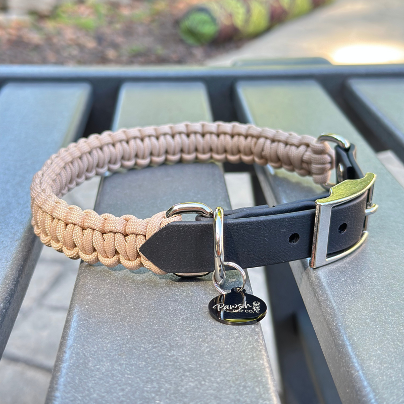 Dog collar with a light tan braided design and black biothane strap on a blue surface.