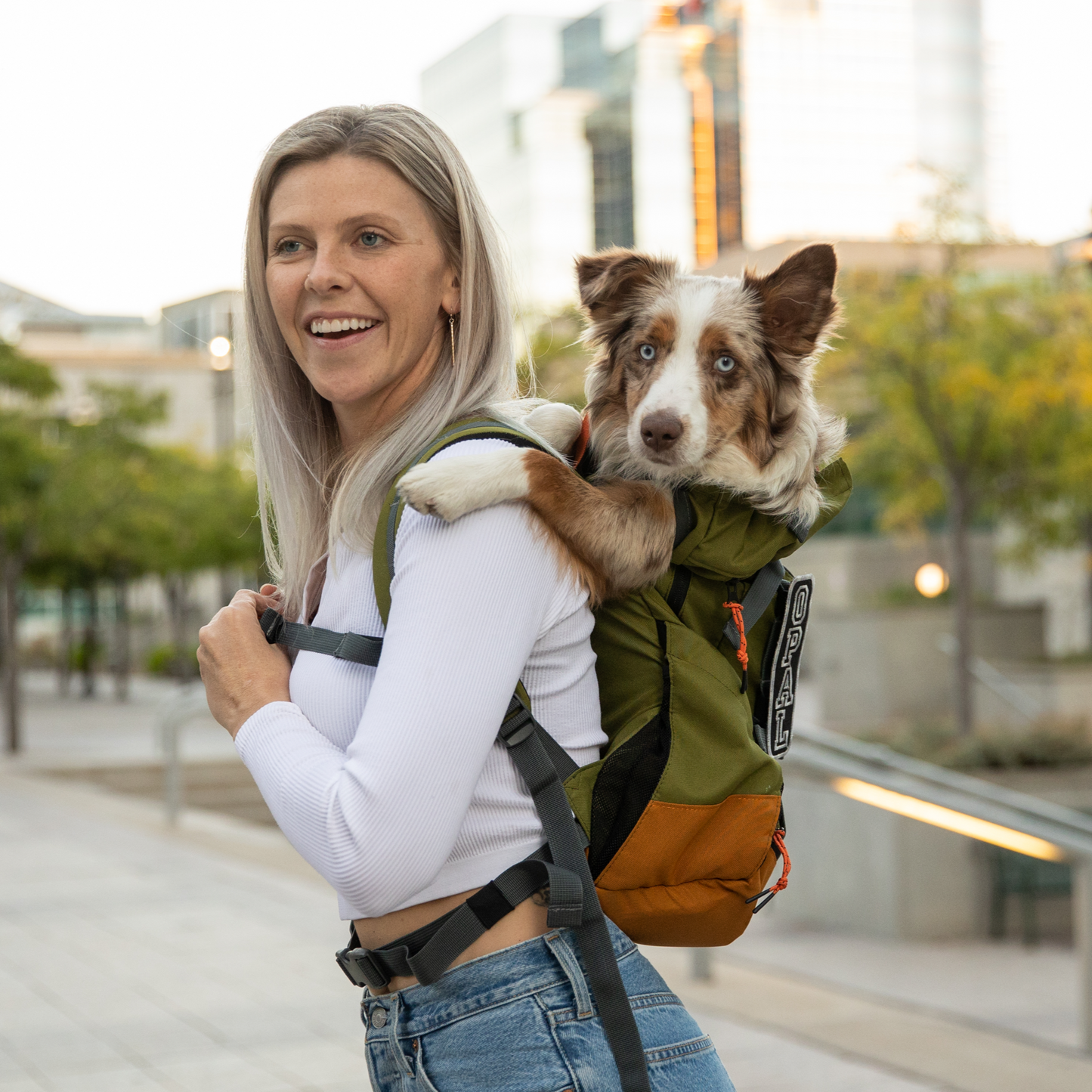 Woman carrying a dog in a backpack with a cityscape background