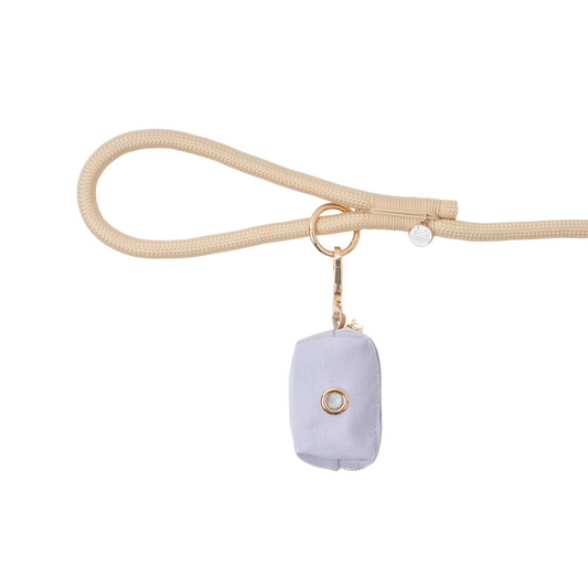 Lavender dog poop bag with gold ring on a beige strap against a white background