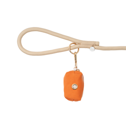 Beige dog leash with an orange bag attachment on a white background