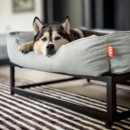 Dog lying on a gray pet bed with a FUZI logo in a home setting