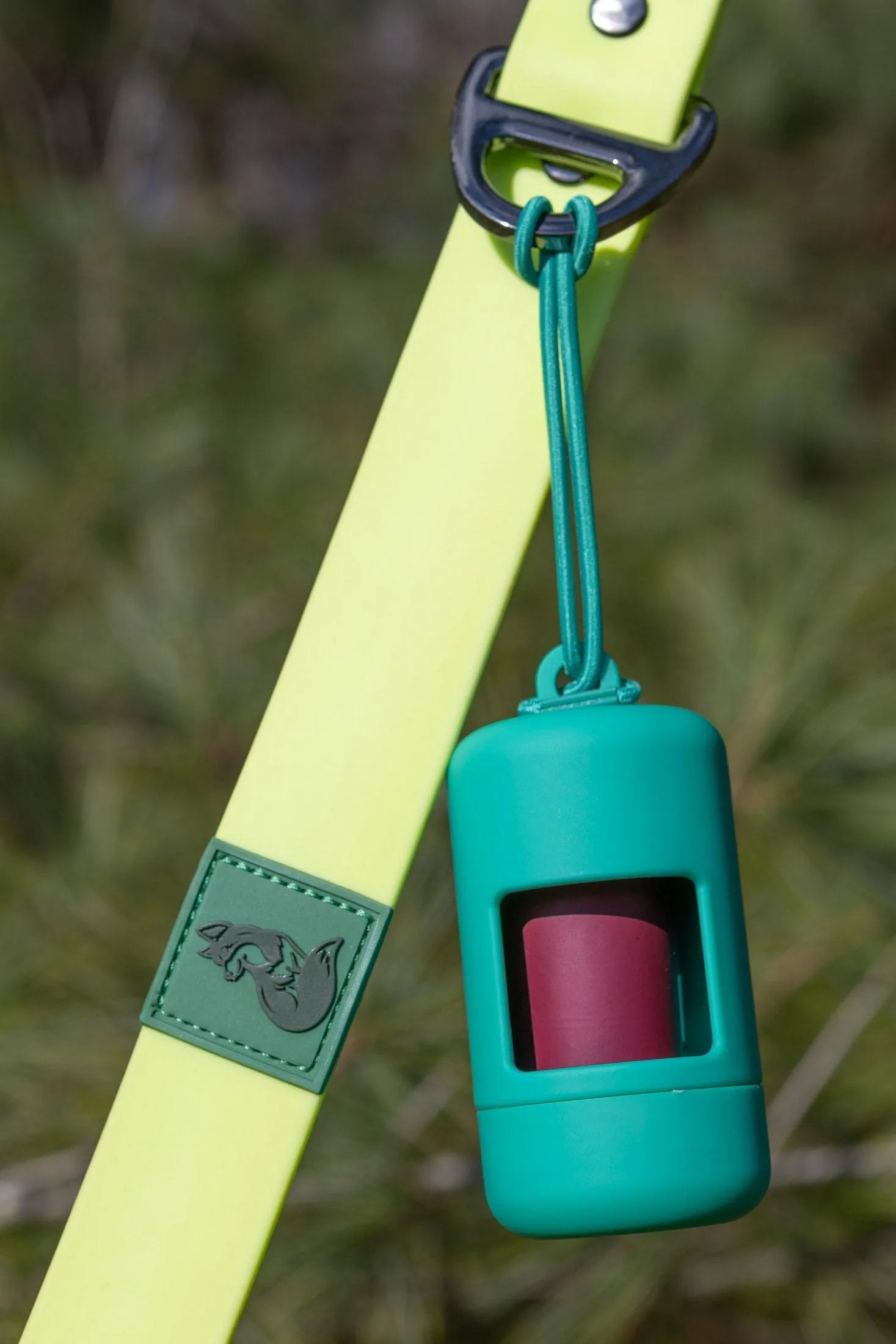 Green dog waste bag holder attached to a yellow leash with grass in the background