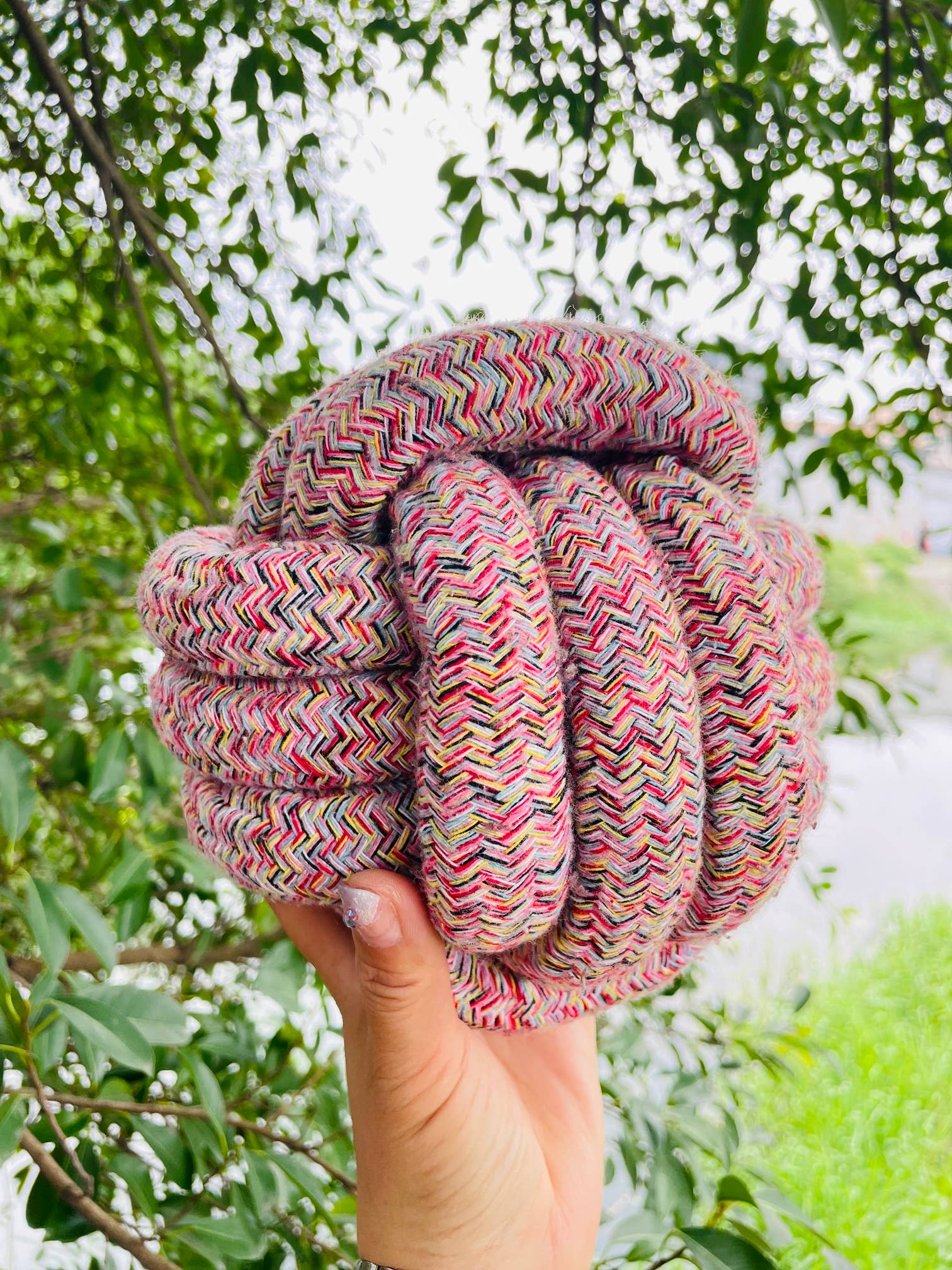 Hand holding a colorful knotted rope against a natural background