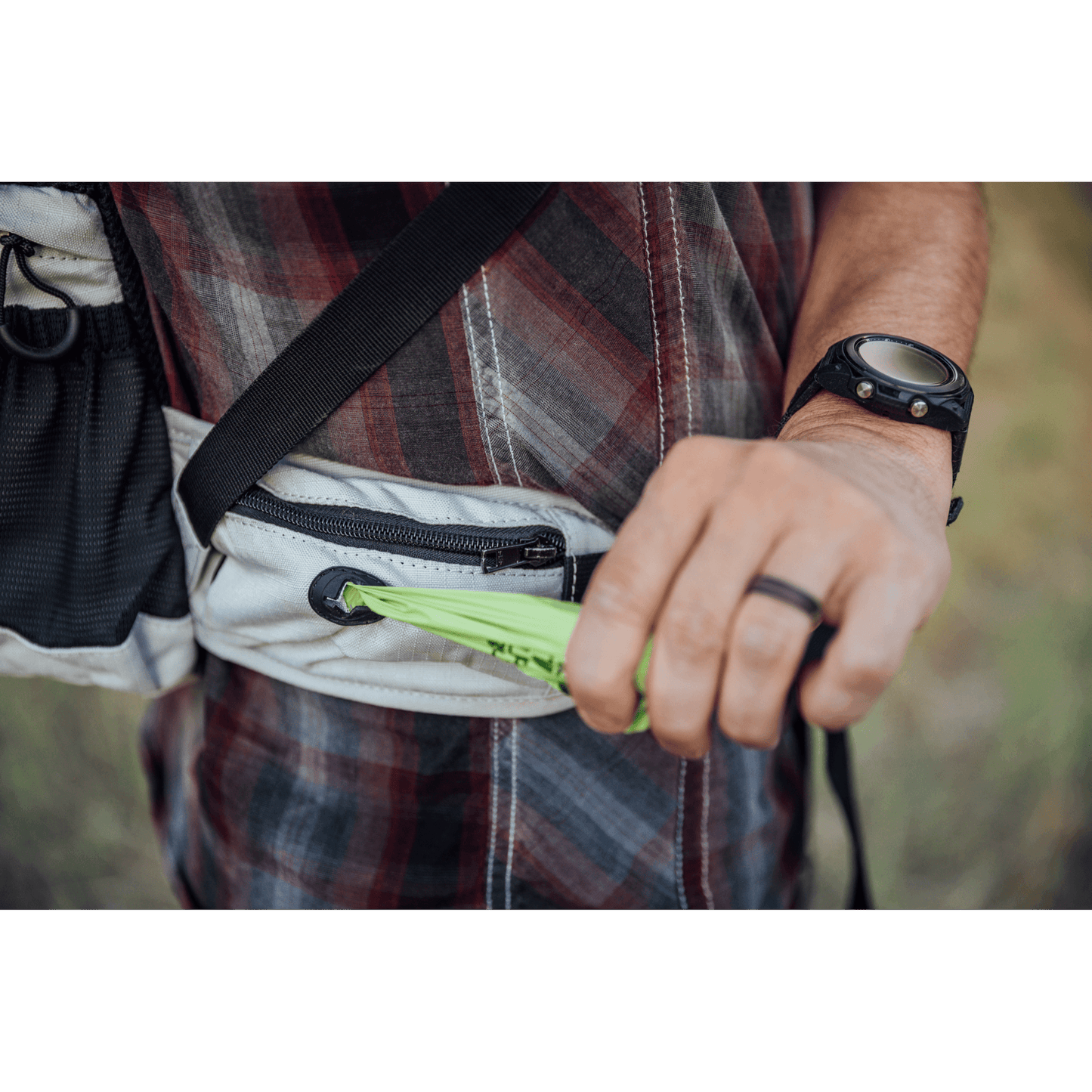 Person holding a green object with a plaid shirt and black strap in the background