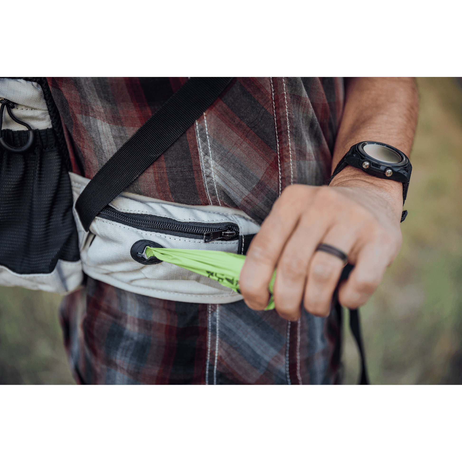 Person holding a green object with a plaid shirt and black strap in the background