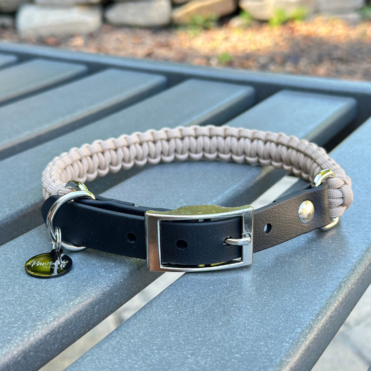 Dog collar with a light tan braided design and black biothane strap  on a blue surface.
