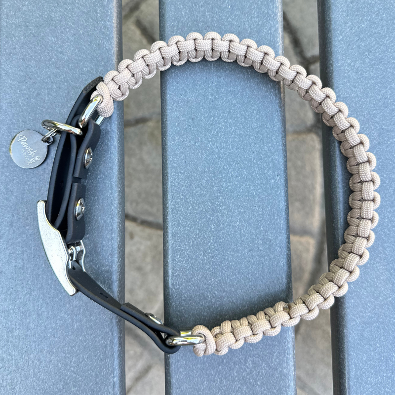 Dog collar with a light tan braided design and black biothane strap  on a blue surface.