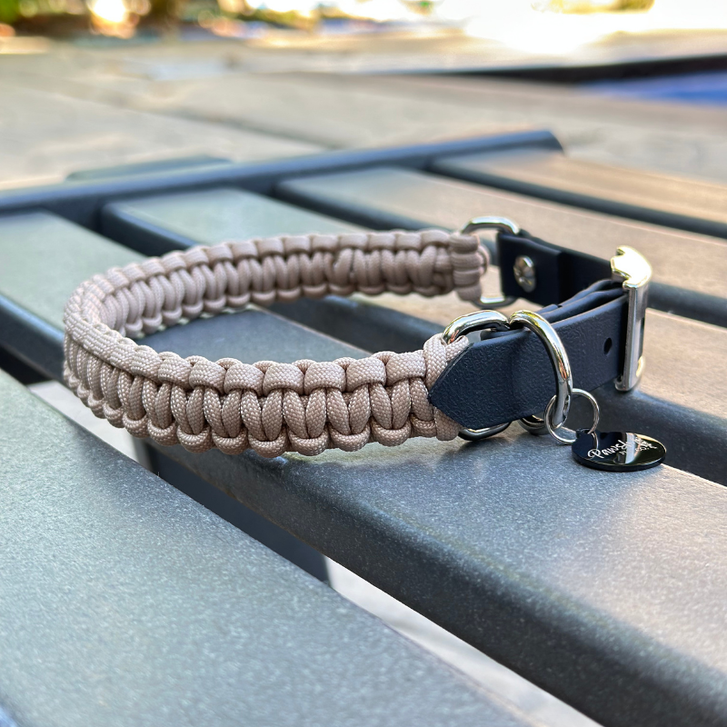 Dog collar with a light tan braided design and black biothane strap  on a blue surface.