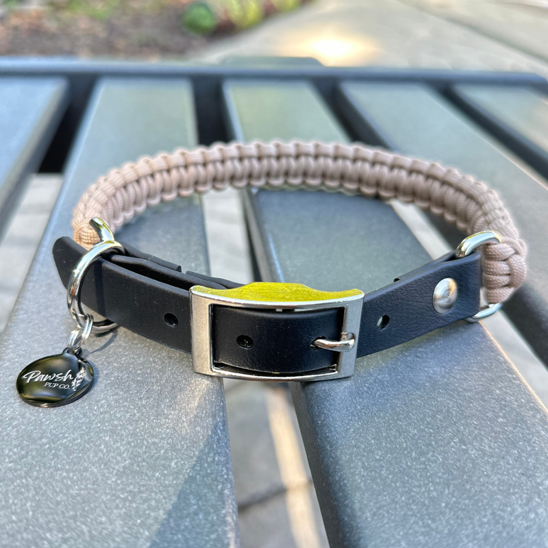 Dog collar with a light tan braided design and black biothane strap  on a blue surface.