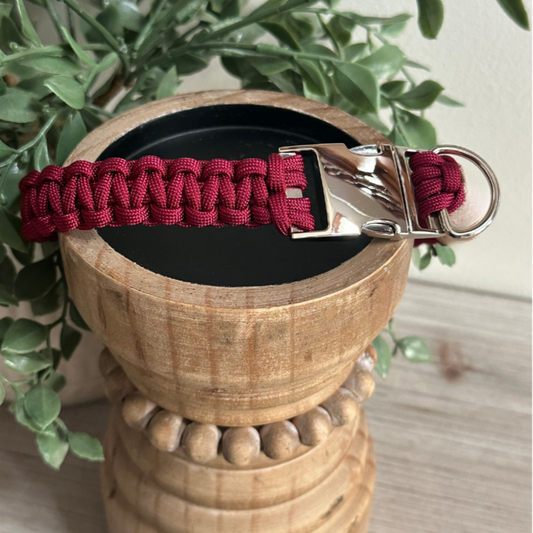 Red paracord keychain on a wooden stand with greenery in the background