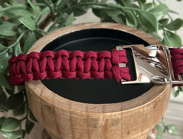 Red paracord dog collar with a silver clasp on a wooden block with a plant in the background