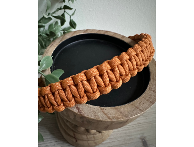 Orange braided dog collar on a wooden planter with a plant in the background