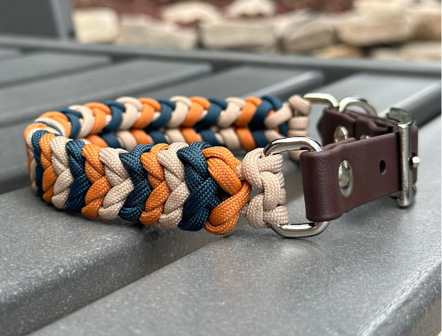 Dog collar with braided design in orange, blue, and beige on a metal surface.
