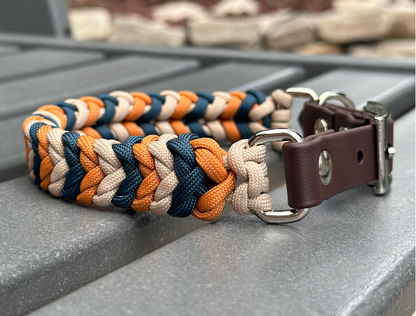 Dog collar with braided design in orange, blue, and beige on a metal surface.