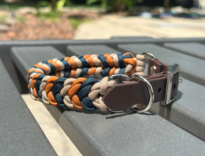 Multicolored braided dog collar with a brown leather patch on a gray surface.