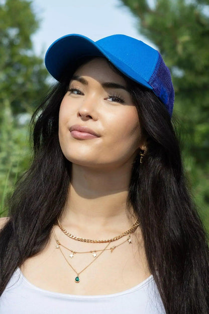 Woman wearing a blue cap and layered necklaces with a blurred green background