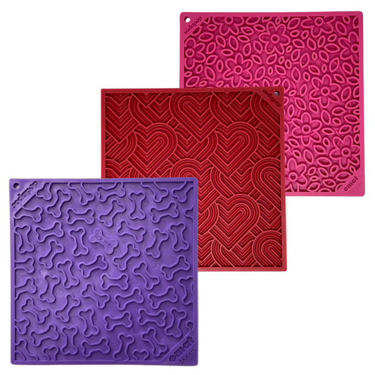 Three silicone dog lick mats in purple, red, and pink with textured patterns on a white background.