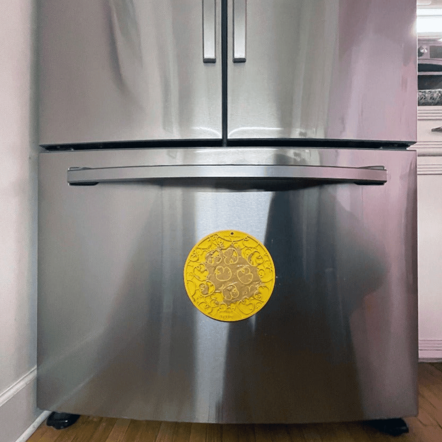Stainless steel refrigerator with a yellow lick mat suction cupped to it on a white wall background