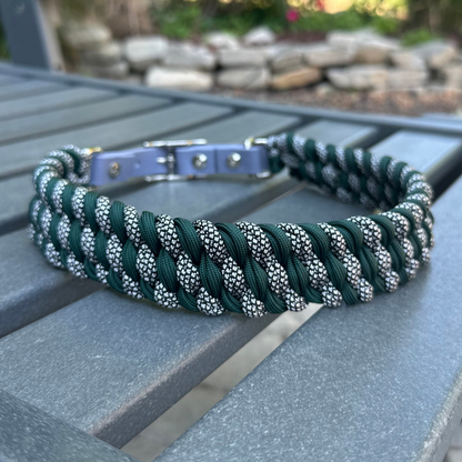 Dog collar with hunter green and silver diamond braided design and gray BioThane strap on a gray surface with a garden background.