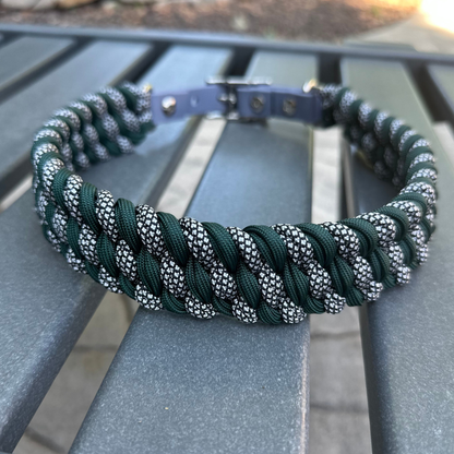 Dog collar with hunter green and silver diamond braided design and gray BioThane strap on a gray surface with a garden background.