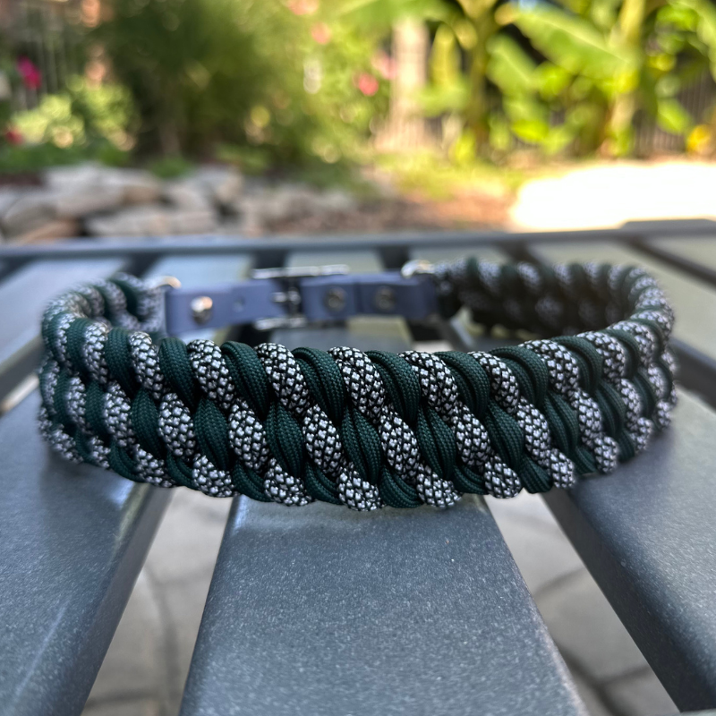 Dog collar with hunter green and silver diamond braided design and gray BioThane strap on a gray surface with a garden background.