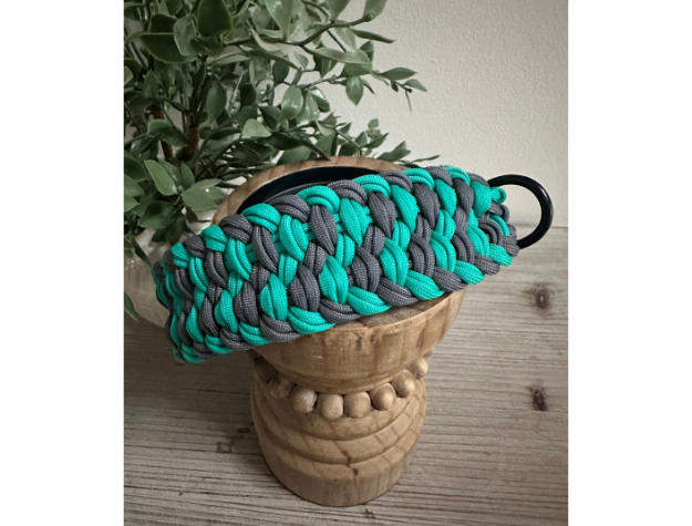 Teal and gray braided dog collar on a wooden stool with a plant in the background