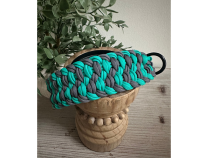 Teal and gray braided dog collar on a wooden stool with a plant in the background