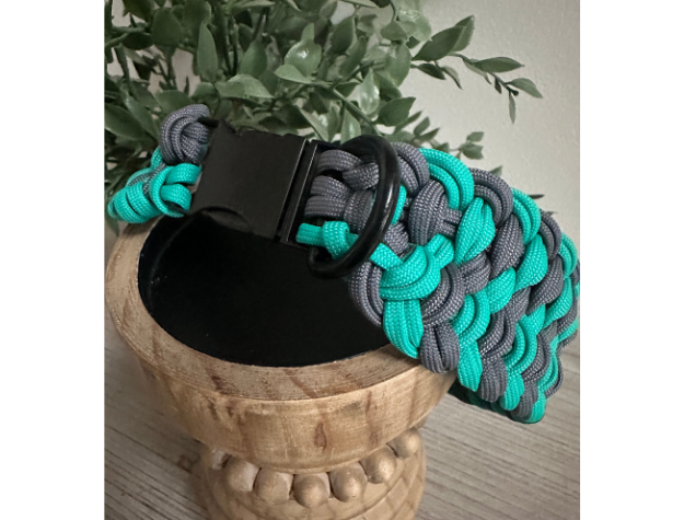 Paracord dog collar with black buckle on a wooden stand with greenery in the background