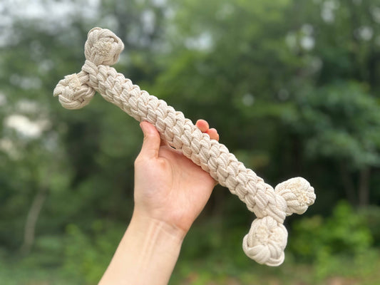 Hand holding a knitted dog toy with a blurred green background
