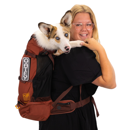 Woman holding a dog in a brown backpack with visible branding on a white background