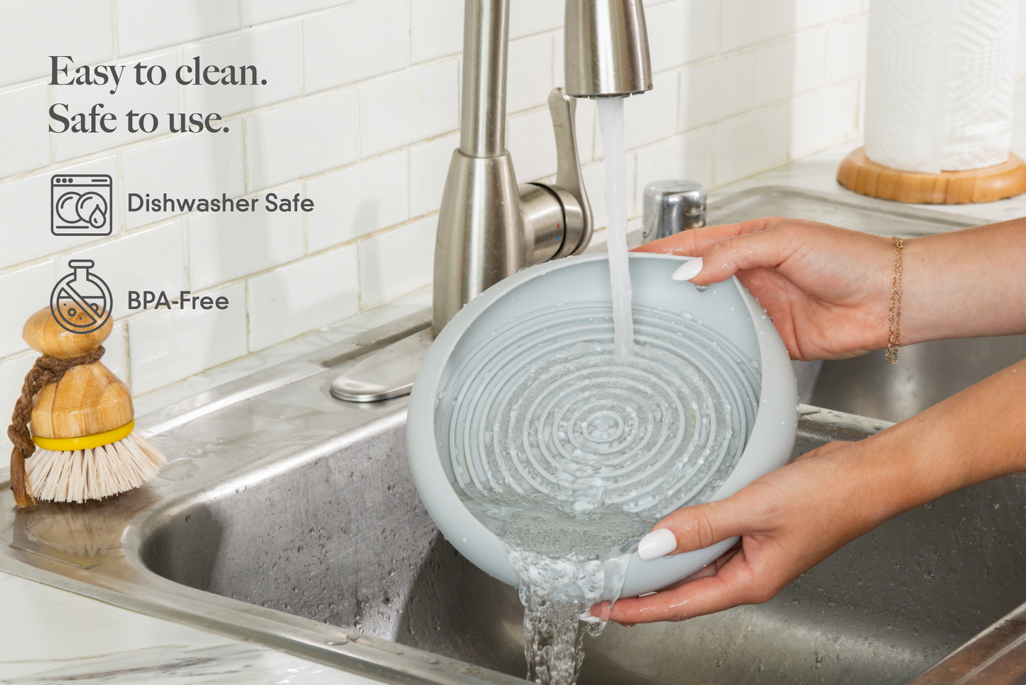 Person washing a gray silicone slow feeder bowl under running water in a kitchen sink.