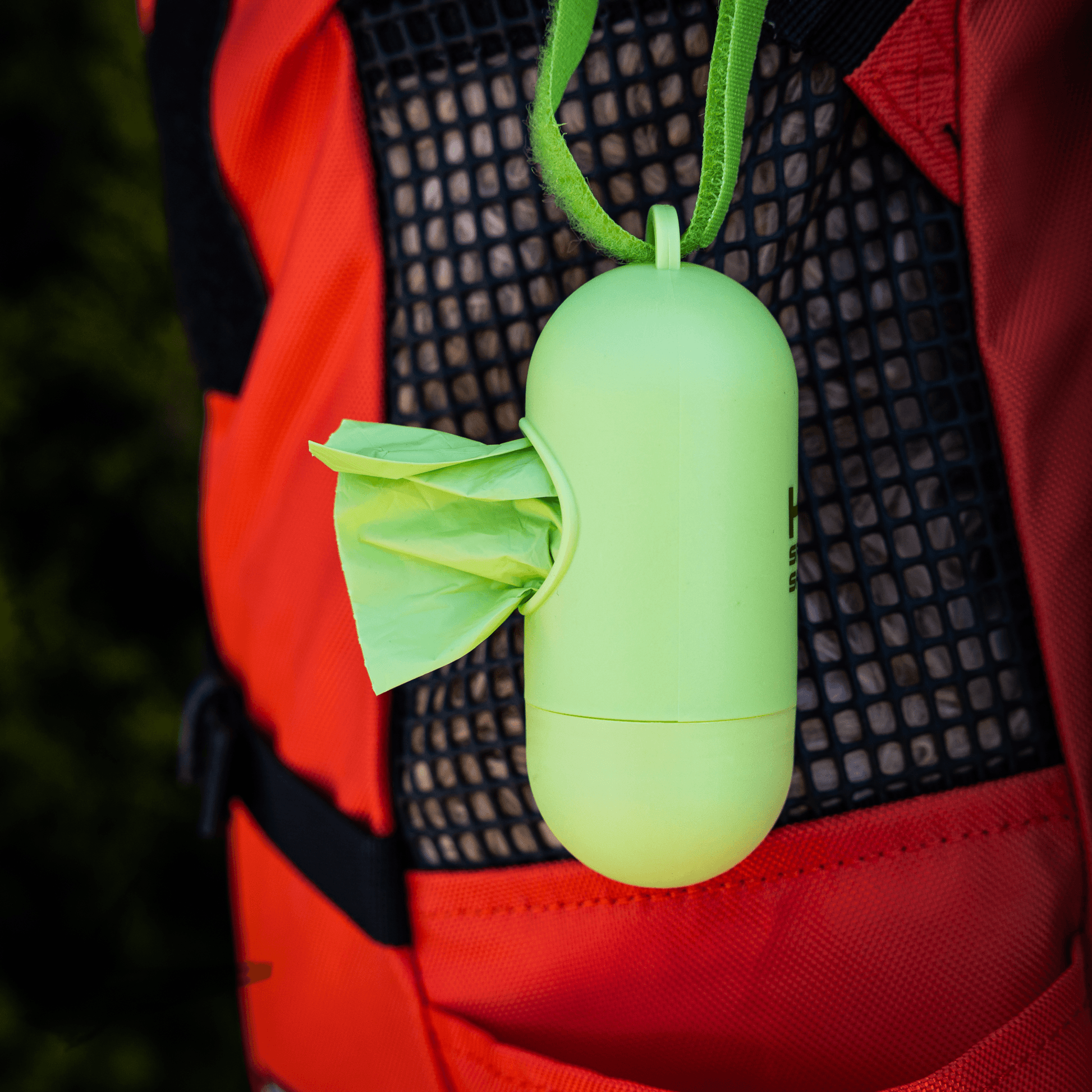 Green portable device with leaf design hanging from a red backpack