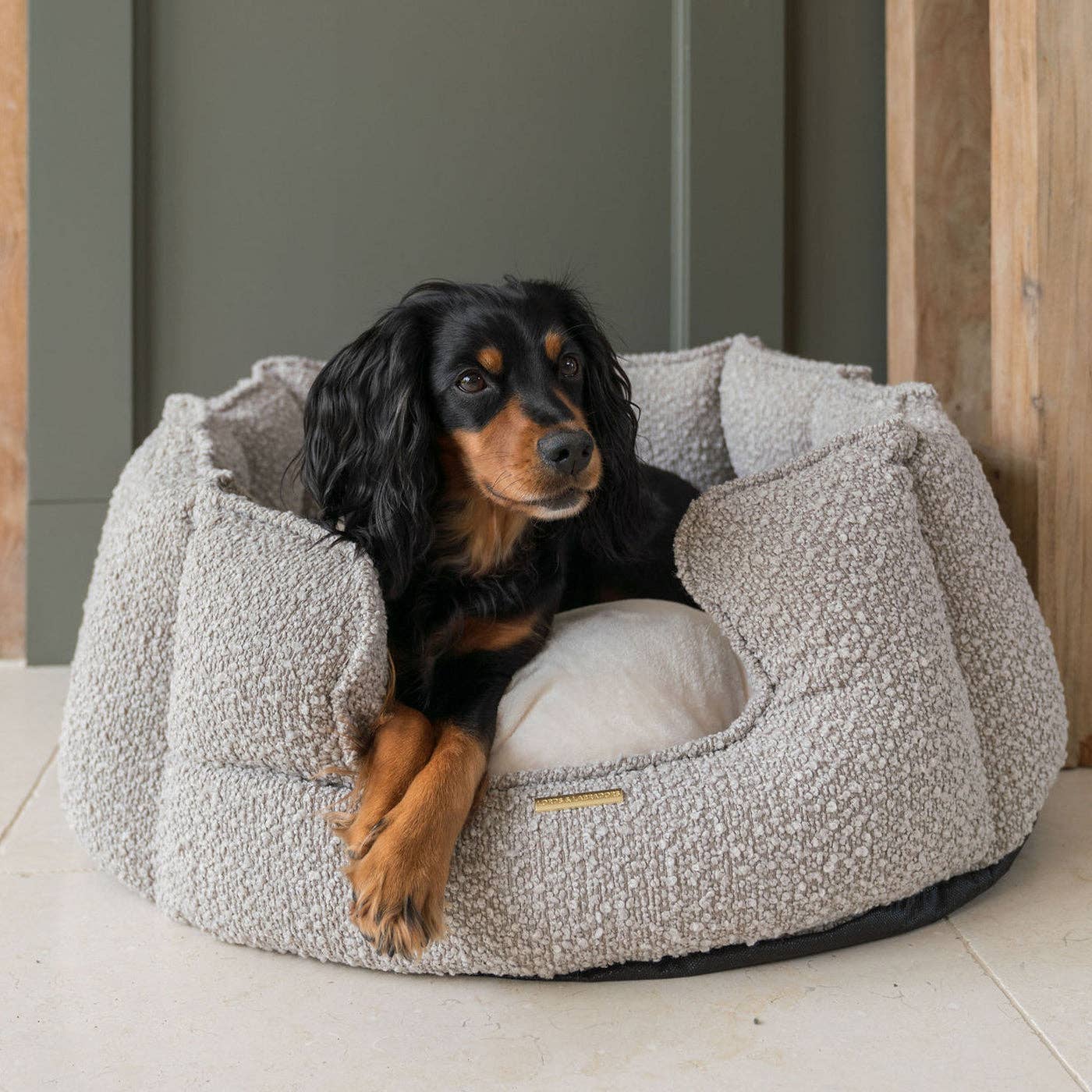 Dog lying in a textured pet bed on a tiled floor.