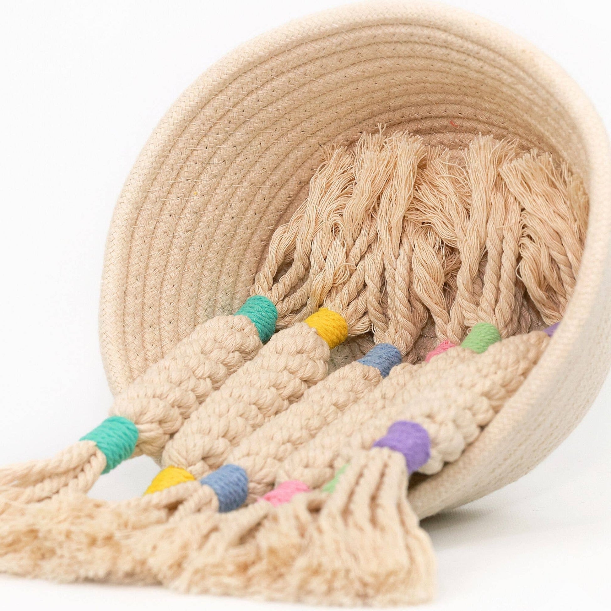 Beige rope dog toys with colorful tassels inside a woven basket on a white background