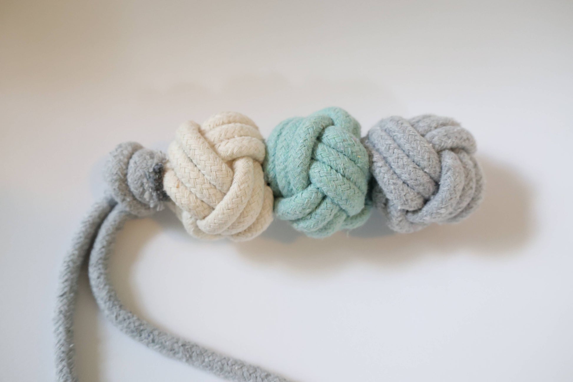 Three knotted rope toys in white, teal, and gray on a light background