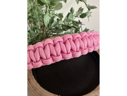 Pink braided dog collar on black decor with green plants in the background