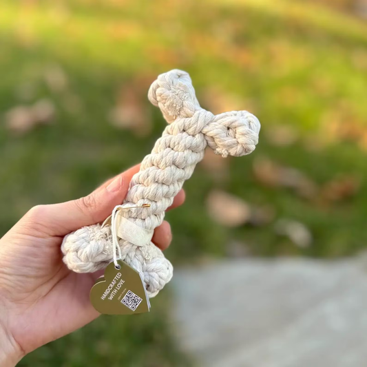 Hand holding a white knotted rope toy with a blurred green background