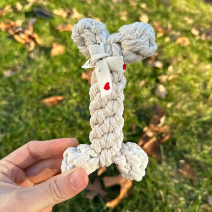 Hand holding a knitted dog toy shaped like a bone with red heart details on grass.