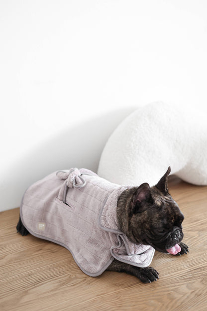 Dog wearing a gray bathrobe on a wooden floor with a white wall in the background