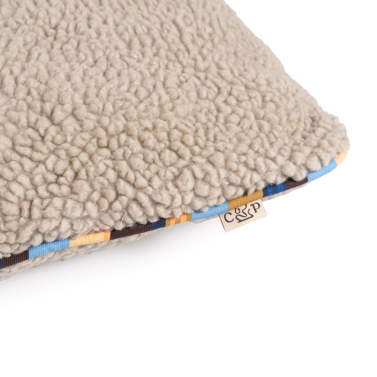 Beige sherpa pillow with a brand tag on a white background