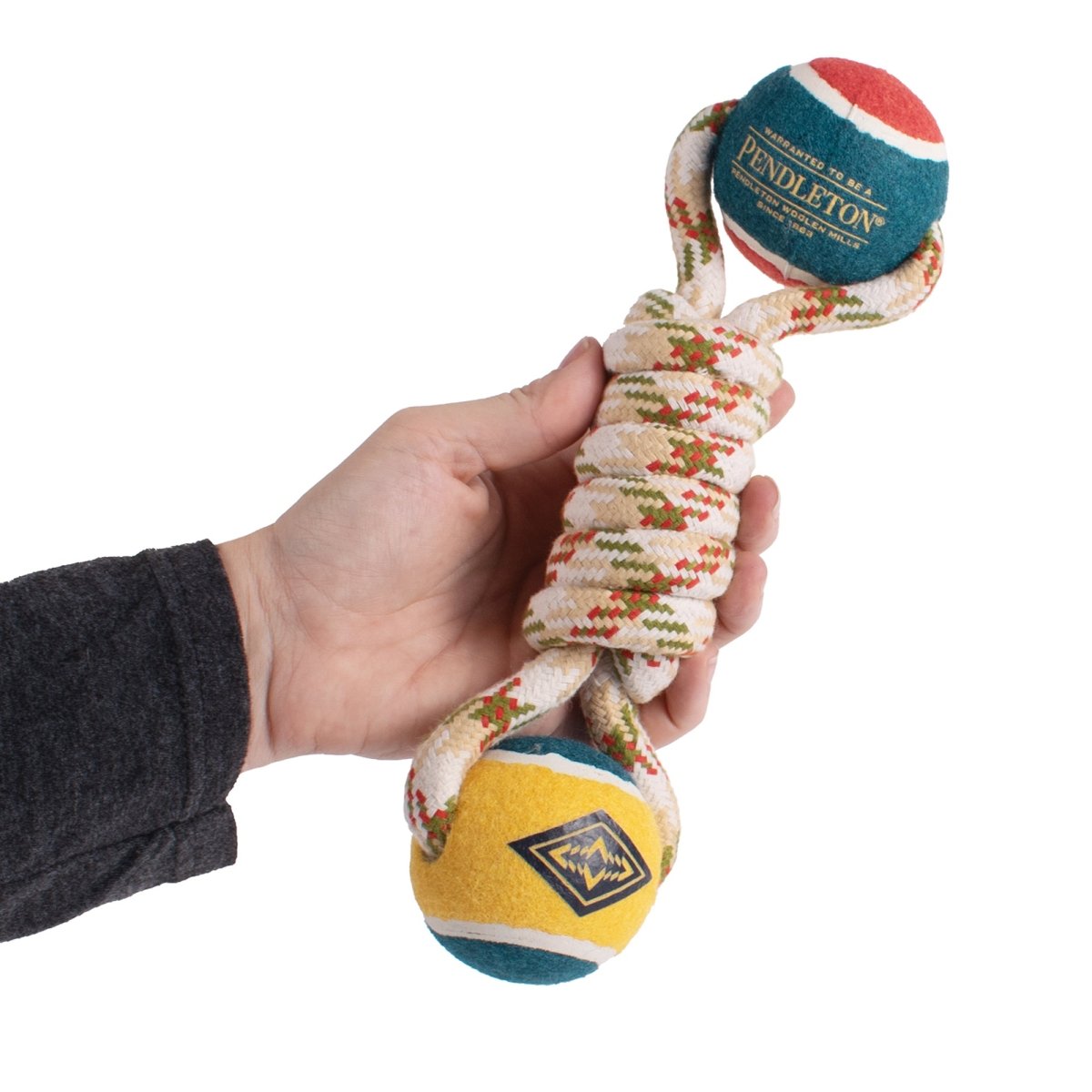 Hand holding a dog toy with colorful balls and knotted rope on a white background