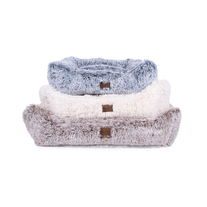 Stack of three fluffy pet beds in gray, white, and brown on a white background